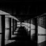 A striking black and white image capturing a lone cyclist under a series of concrete pillars.